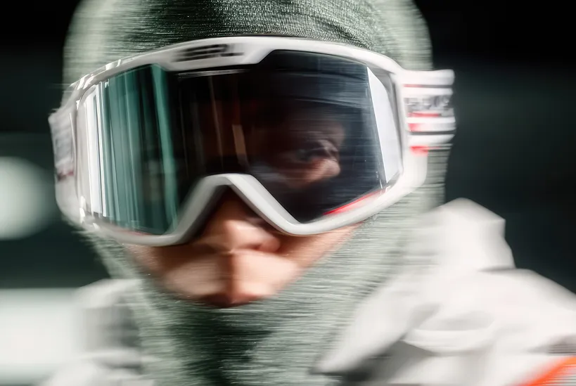 Close-up of a person wearing a gray balaclava and large reflective ski goggles.