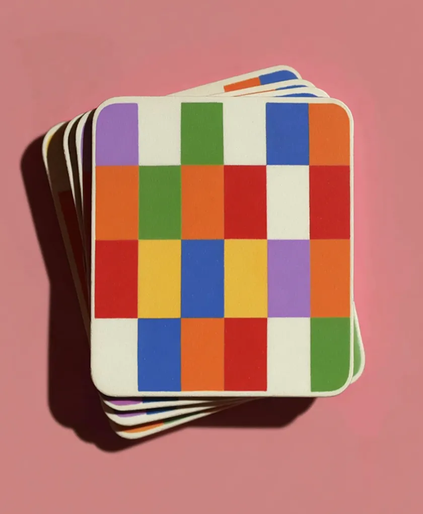 Stack of square coasters with a colorful geometric pattern of rectangles in orange, green, purple, blue, red, and yellow on a pink background.