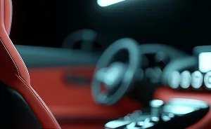 Close-up of a red leather car seat with blurred steering wheel and dashboard in the background.